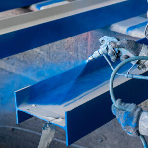 A man applies blue spray paint to metal parts during spray painting services on metal