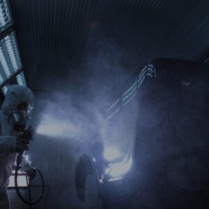 A man in a white suit uses spray painting services of Precision Powder Coating to apply a fresh, even coat of paint to a car